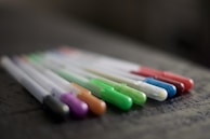 Close-up of colorful pens and markers laid out on a wooden desk.