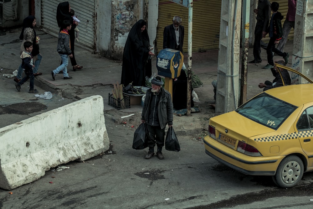 昼間、黄色い車の脇に立つ黒いヒジャブをかぶった女性