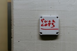 A white wall-mounted device displays a message written in red lettering, expressing a strong sentiment against law enforcement.