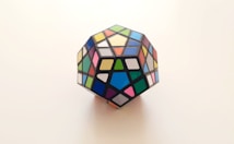 A multicolored dodecahedron puzzle featuring various geometric shapes on each face. The puzzle is displayed against a plain, light-colored background, emphasizing its vibrant colors.