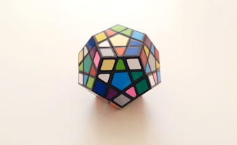 A multicolored dodecahedron puzzle featuring various geometric shapes on each face. The puzzle is displayed against a plain, light-colored background, emphasizing its vibrant colors.