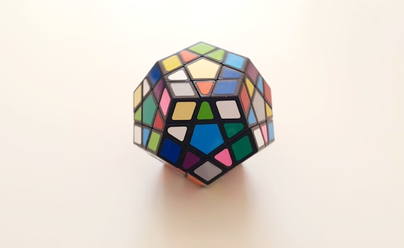 A multicolored dodecahedron puzzle featuring various geometric shapes on each face. The puzzle is displayed against a plain, light-colored background, emphasizing its vibrant colors.