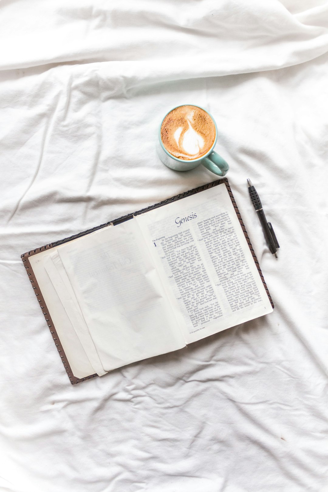 white book beside black click pen on white textile