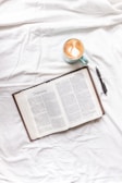 An open devotional book resting on a creamy neutral linen cloth beside a steaming cup of tea.