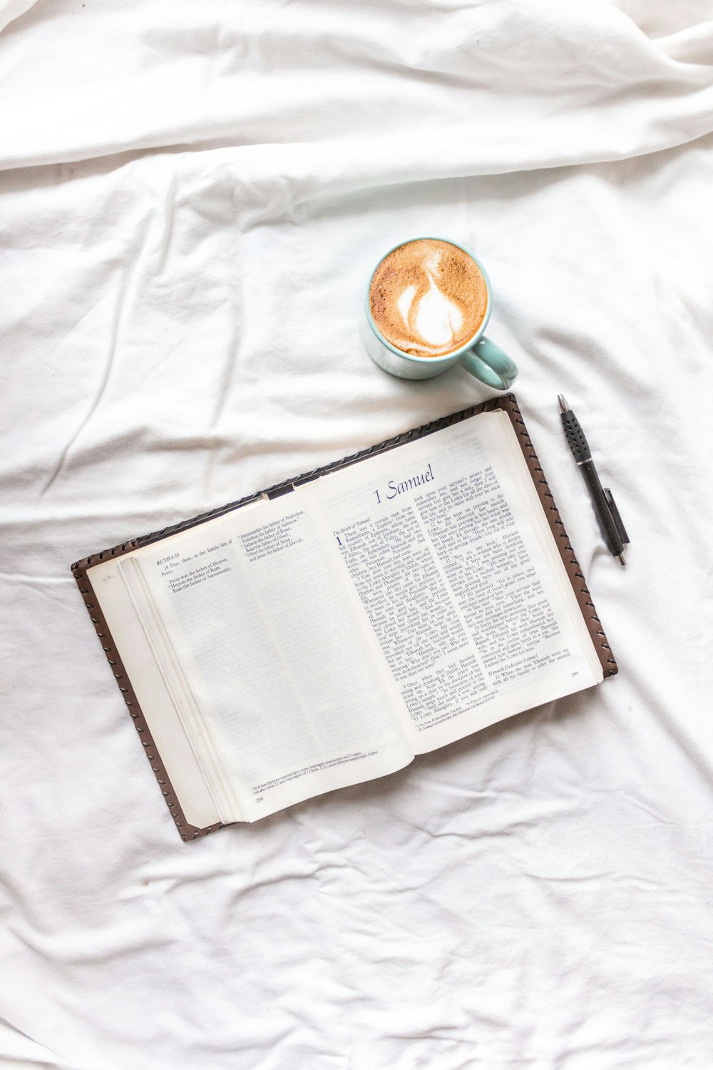 black click pen on white book page beside white ceramic mug with coffee