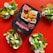A package of plant-based nuggets is centered on a vibrant red background, surrounded by three taco-like servings filled with salad, avocado, and crispy nuggets. The package features bold text indicating the product is soya based and gluten-free.