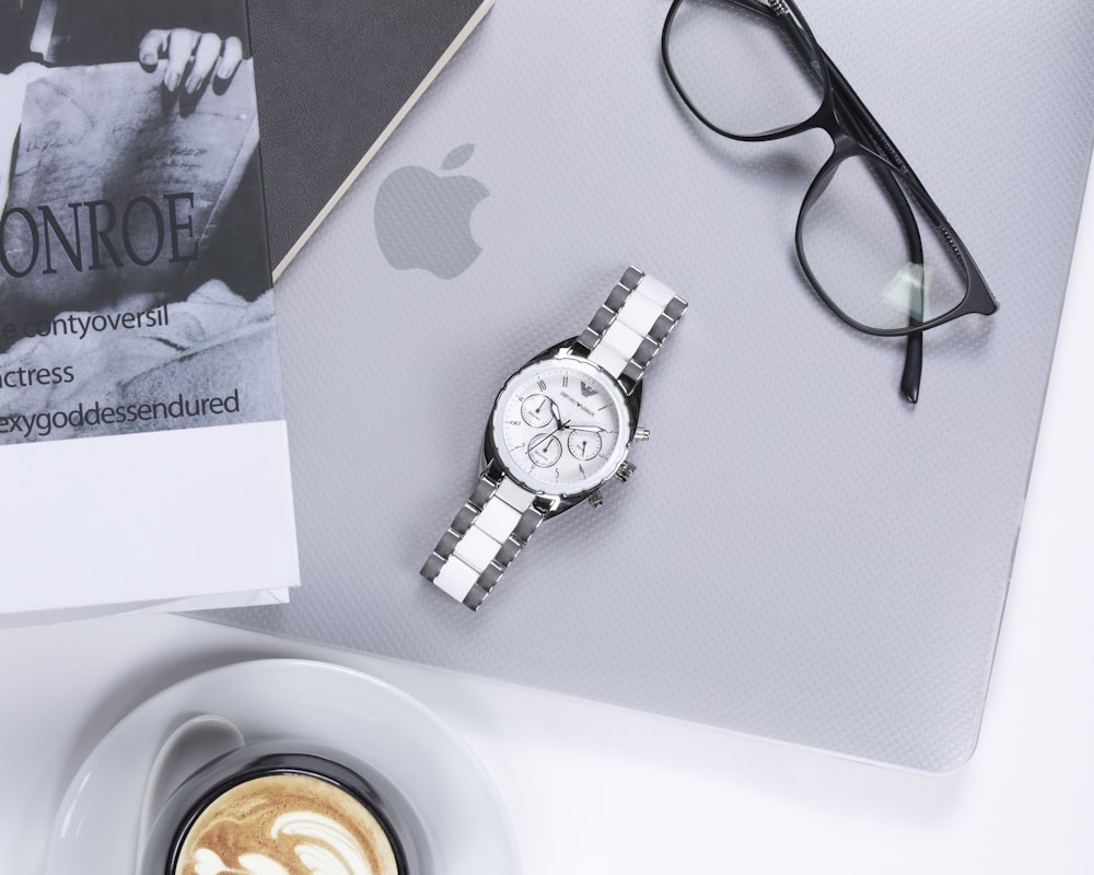 black framed eyeglasses beside silver round analog watch