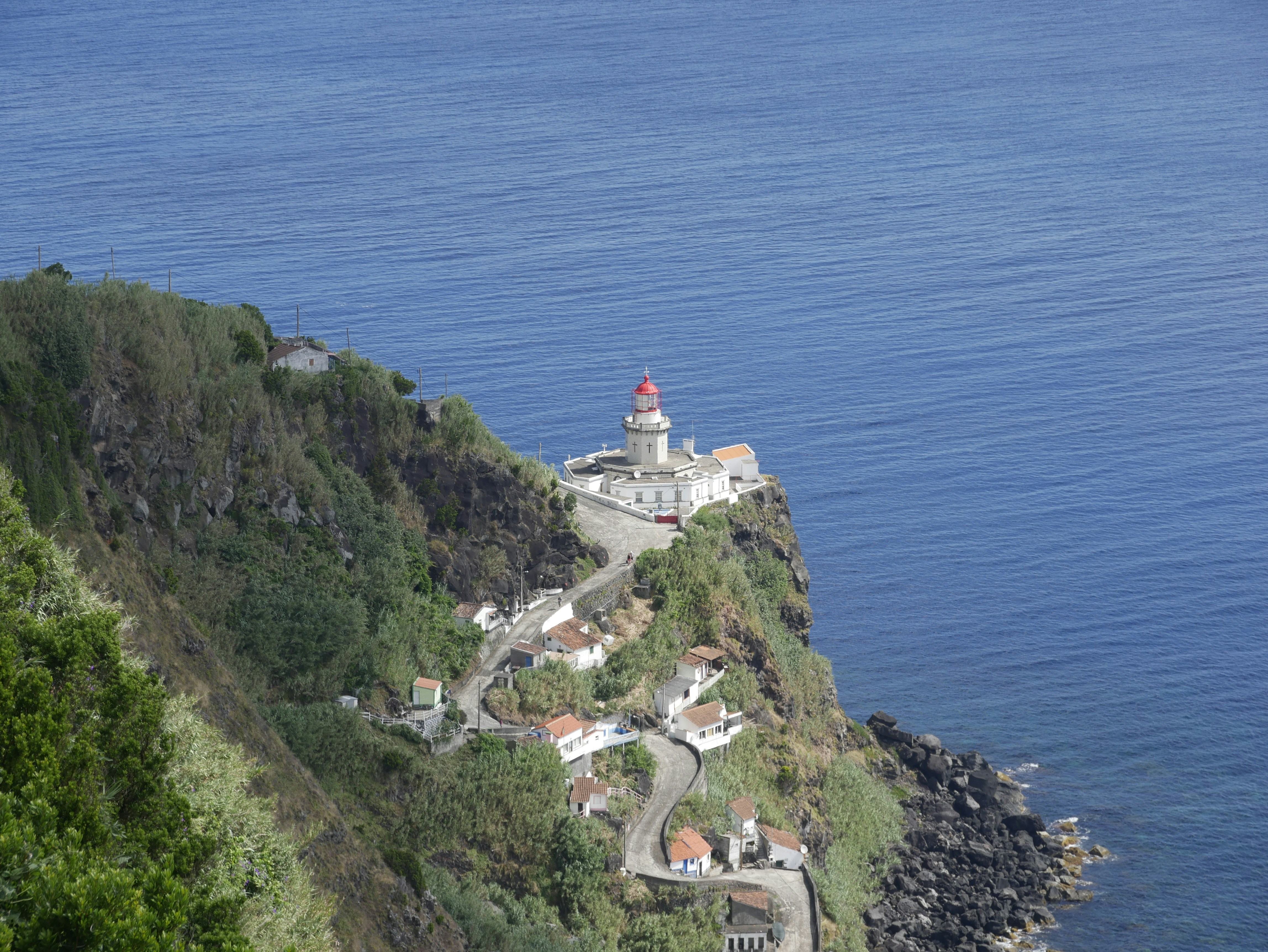 white and red lighthouse on cliff by the sea during daytime