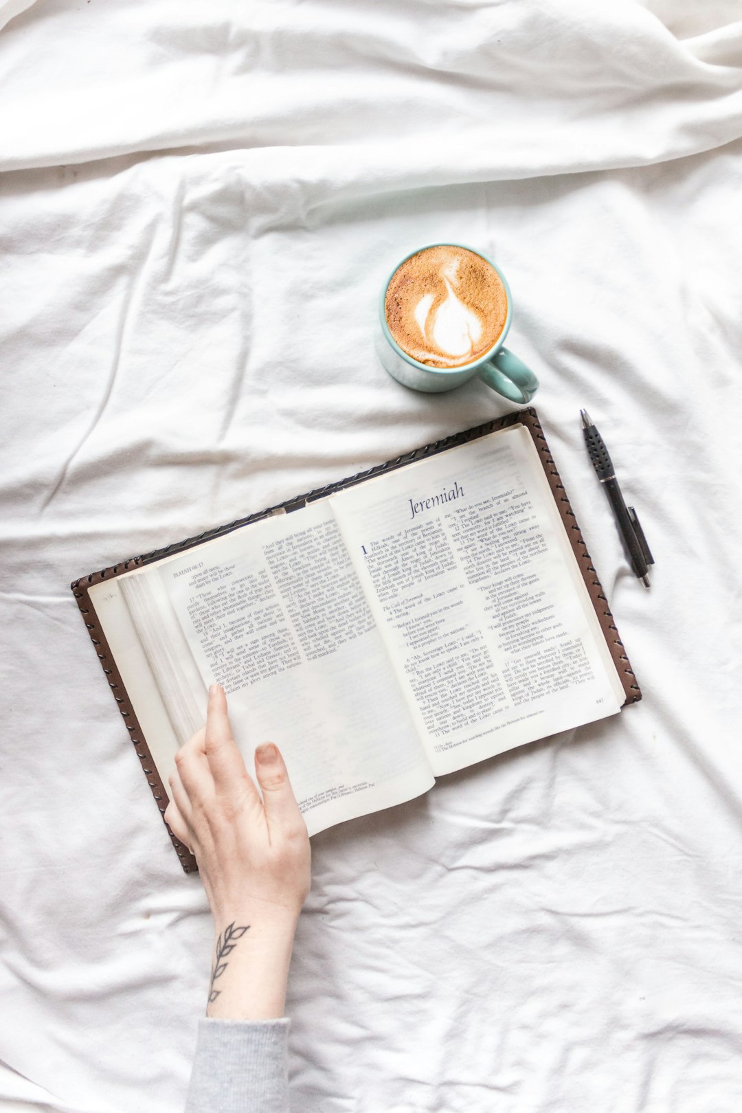 person reading book on white bed linen