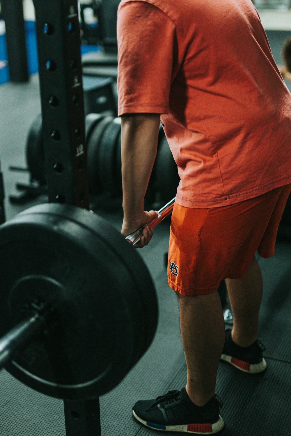 man in orange t-shirt and red shorts carrying black barbell