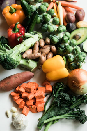 Assorted fresh vegetables including broccoli, peppers, brussels sprouts, and potatoes on a white surface