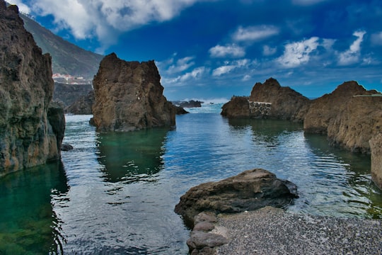 brown rocky mountain beside blue sea under blue sky and white clouds during daytime in Piscinas Naturais de Porto Monìz Portugal