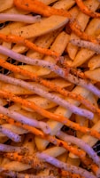 A close-up of crinkle-cut fries arranged neatly, topped with generous servings of two sauces, one white and one orange, and sprinkled with herbs and spices.