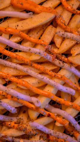 A close-up of crinkle-cut fries arranged neatly, topped with generous servings of two sauces, one white and one orange, and sprinkled with herbs and spices.