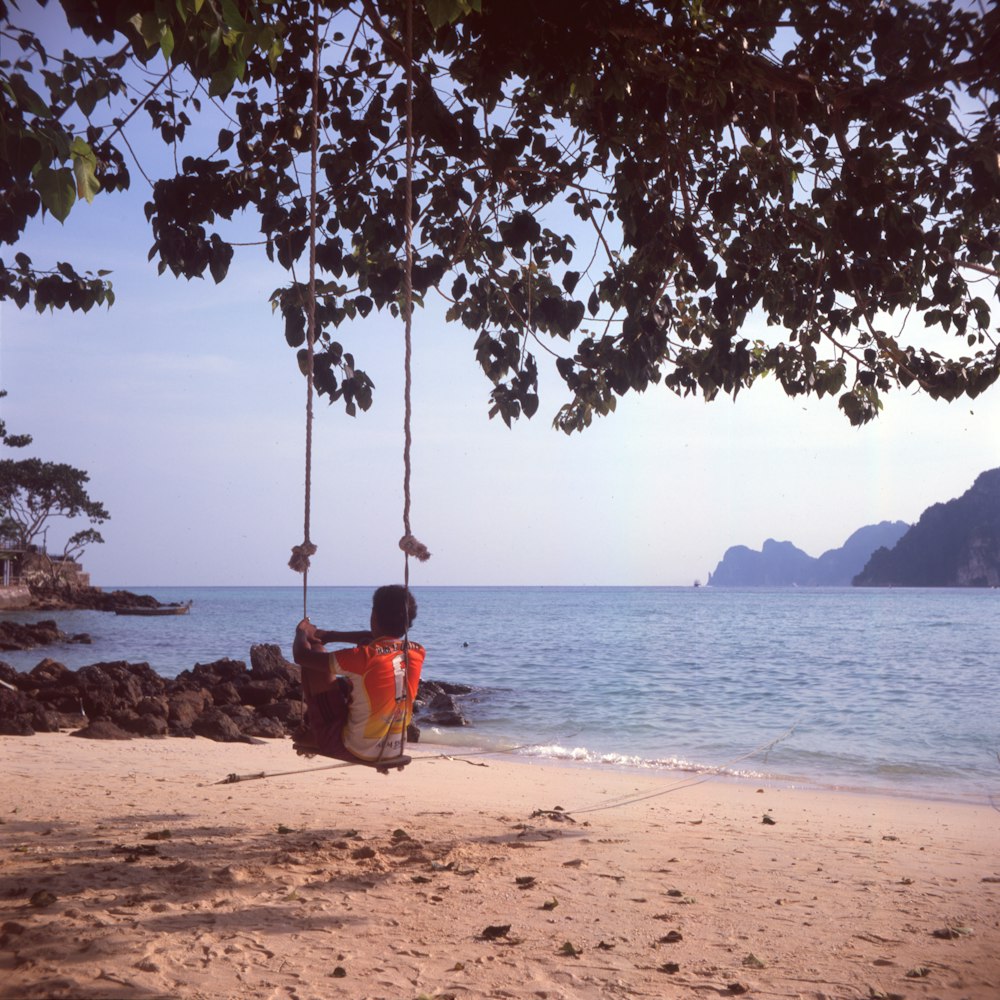 woman in red shirt sitting on swing near body of water during daytime