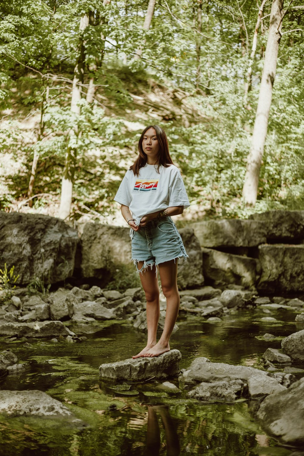 woman in white shirt standing on rock near river during daytime