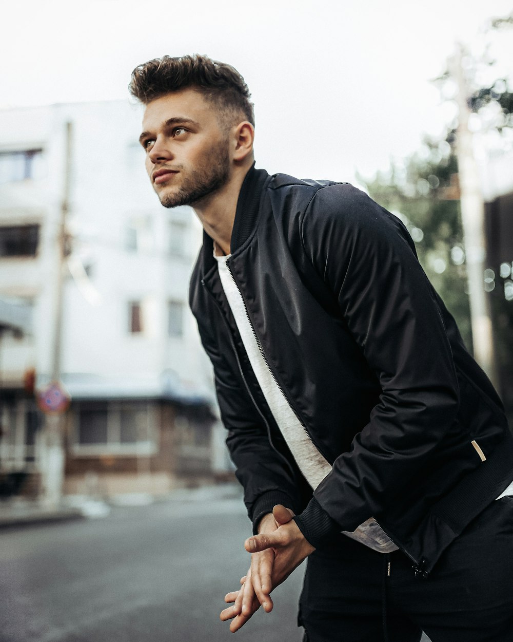 man in black jacket and black pants sitting on sidewalk during daytime