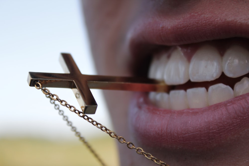 gold crucifix pendant necklace in persons mouth
