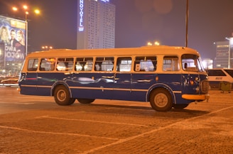 A classic vintage bus from the 1950s parked beside a modern luxury vehicle against the New Delhi skyline.