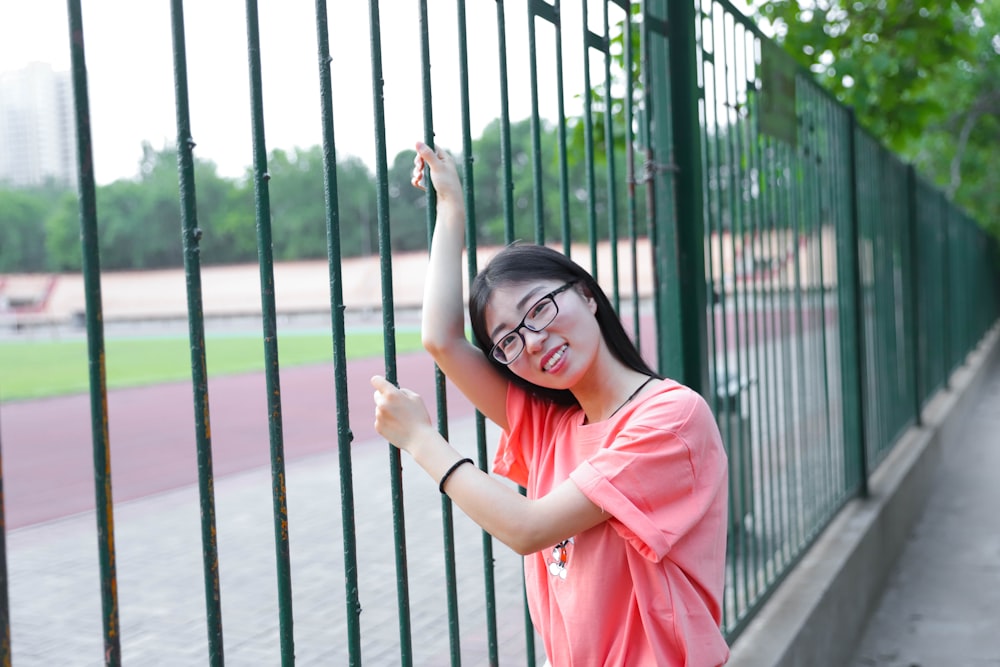 woman in pink long sleeve shirt standing beside black metal fence during daytime