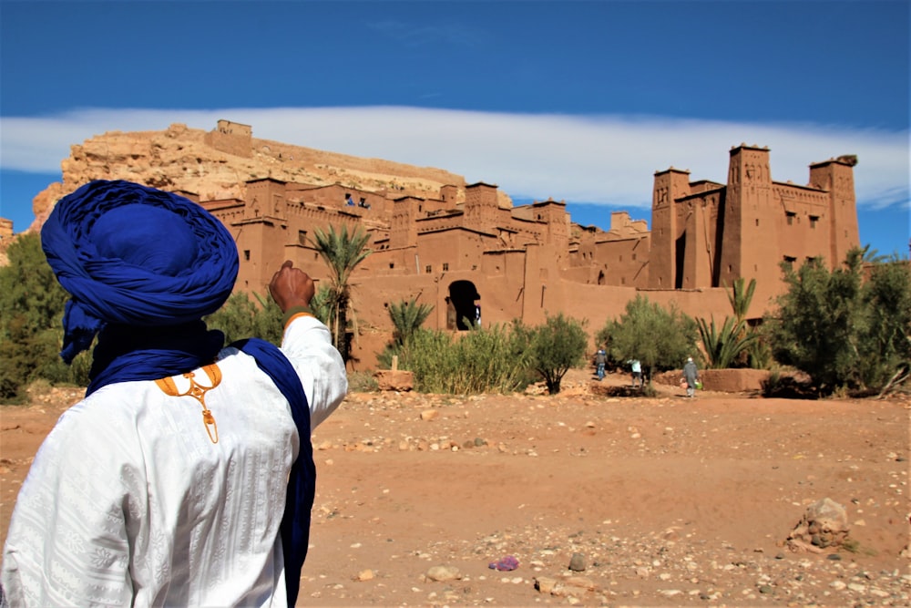 昼間、白い長袖シャツと青い帽子をかぶった人が茶色の砂の上に立っている
