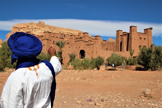 person in white long sleeve shirt and blue hat standing on brown sand during daytime in Ouarzazate Morocco