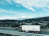 A cargo truck driving along a scenic highway with mountains in the background