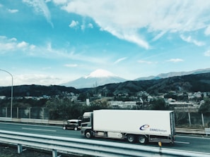 A truck driving along a scenic highway with mountains in the background.