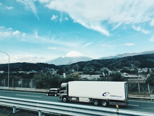 An Elilog Transportes truck driving along a scenic highway with mountains in the background.