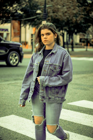 A stylish man wearing a casual denim jacket walking down a city street.