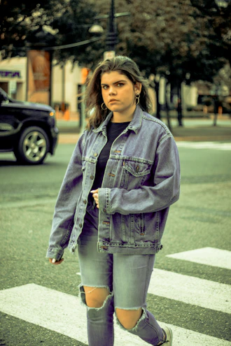 A stylish man wearing a casual denim jacket walking down a city street.