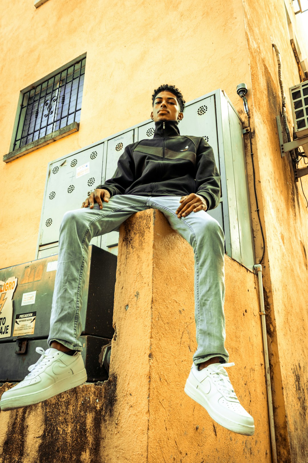 man in black jacket and gray pants sitting on brown concrete wall during daytime