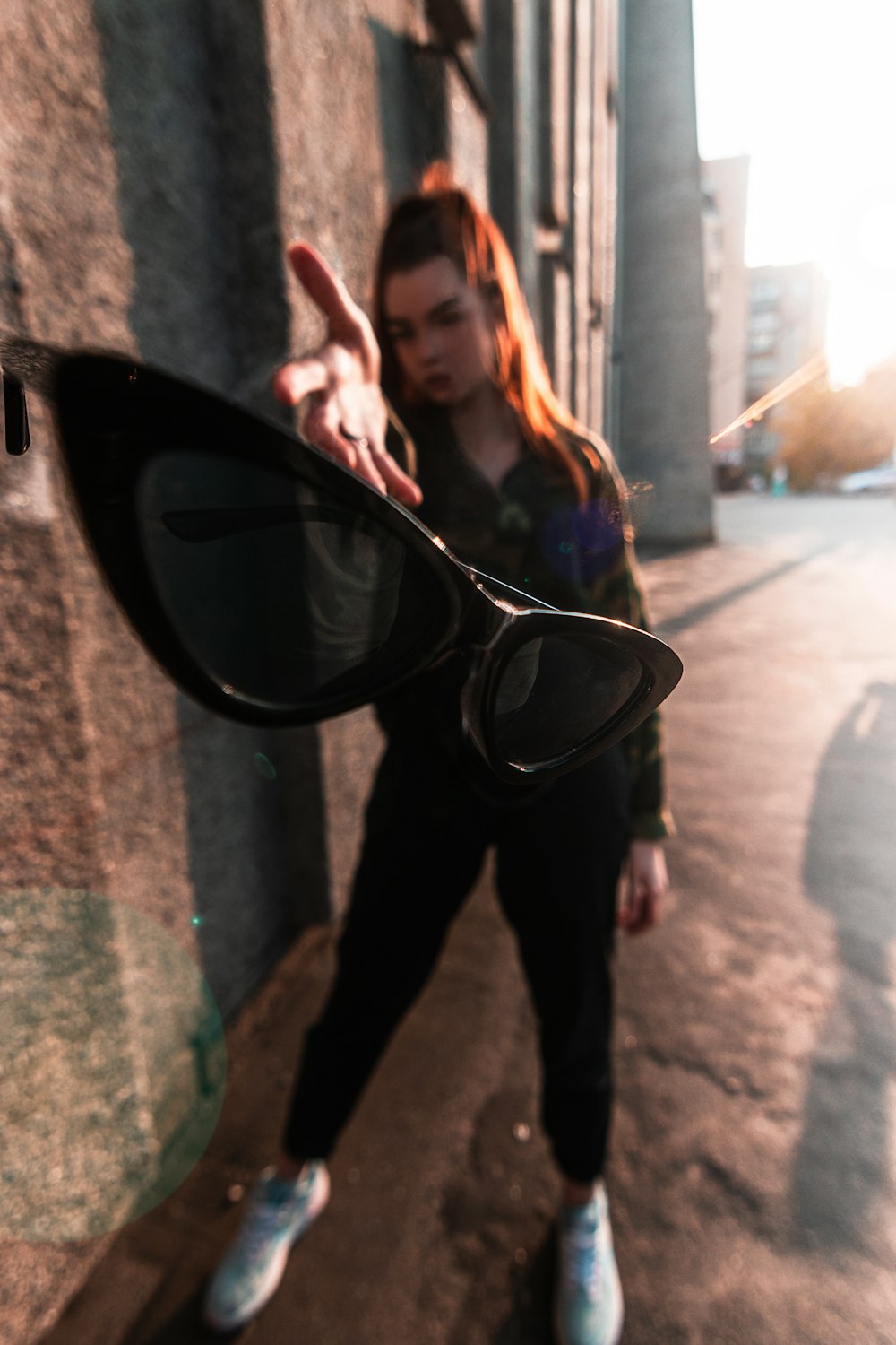 woman in black pants and black jacket holding black framed sunglasses