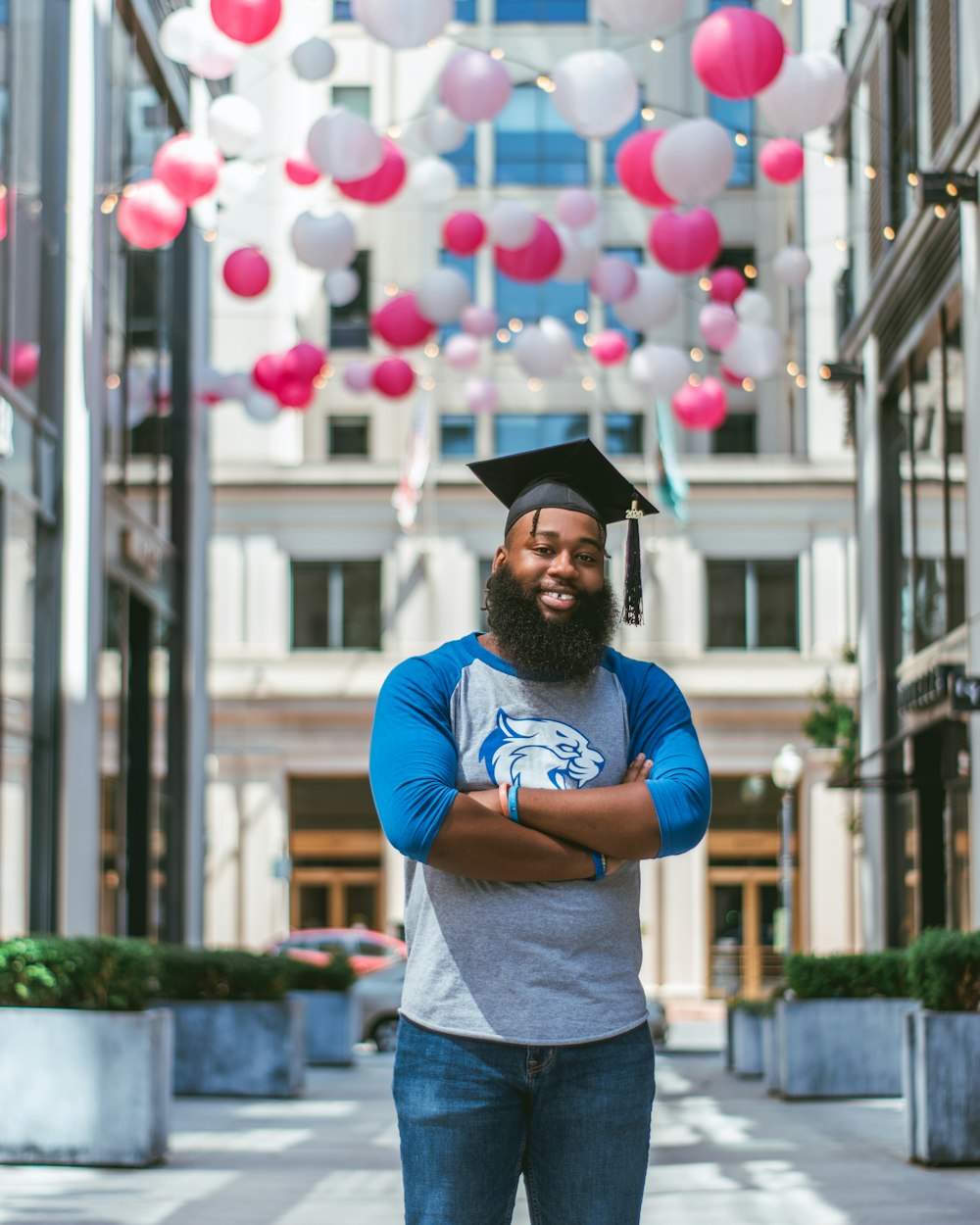 man in blue crew neck t-shirt and blue denim shorts wearing black academic hat standing