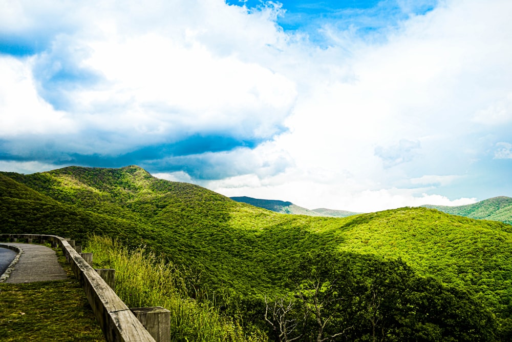 green grass field and mountain under blue sky and white clouds during daytime