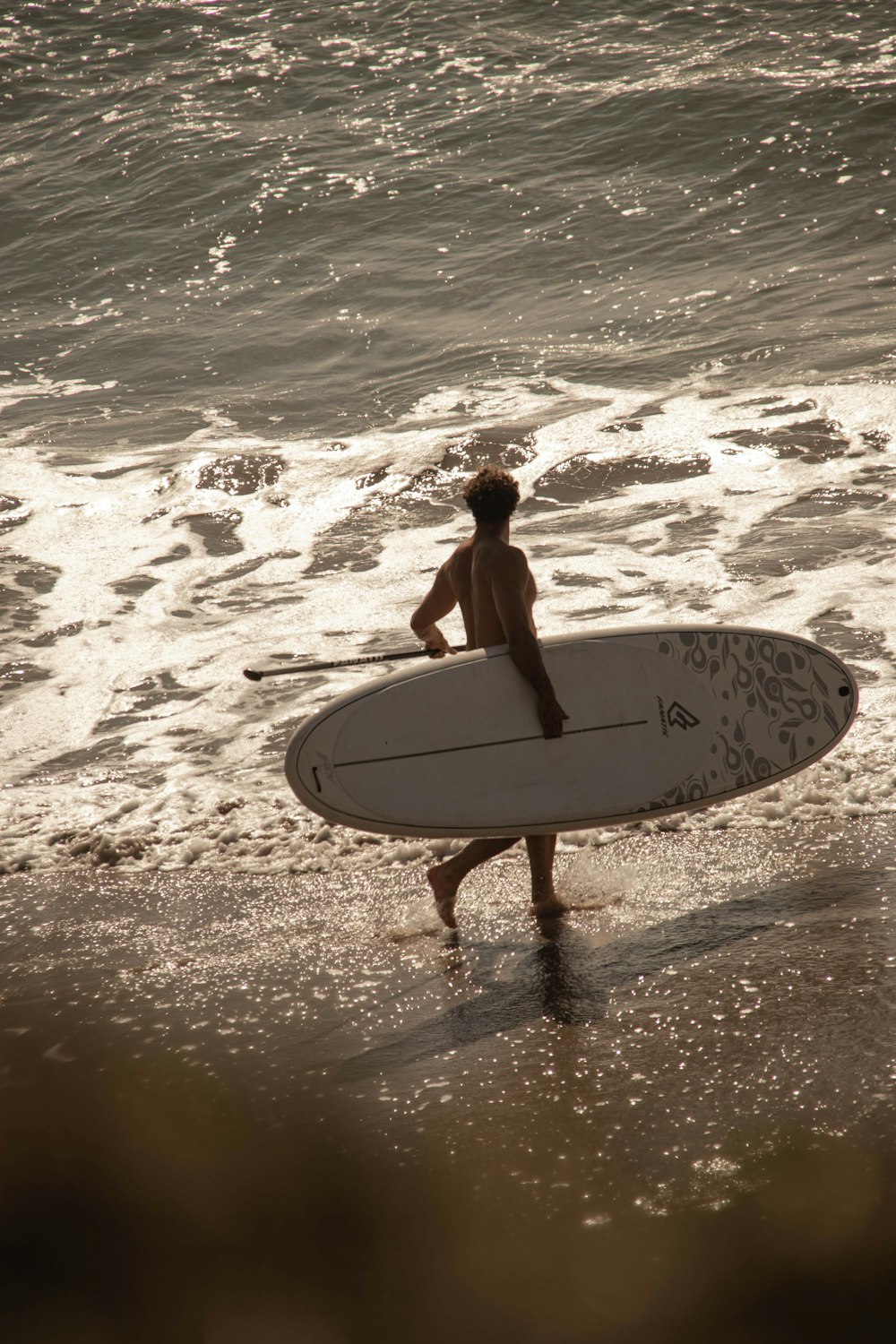 woman in black bikini holding white surfboard walking on beach during daytime
