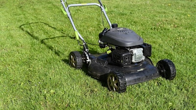 Lawn mower in action on a sunny day, cutting thick green grass.