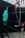 A stethoscope with red tubing is hanging on a black metal fence, and a surgical mask is also hanging next to it slightly blurred in the background.