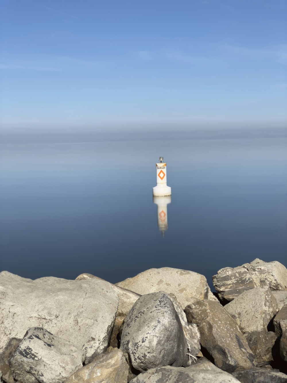 person in white shirt and brown pants standing on gray rock formation near body of water