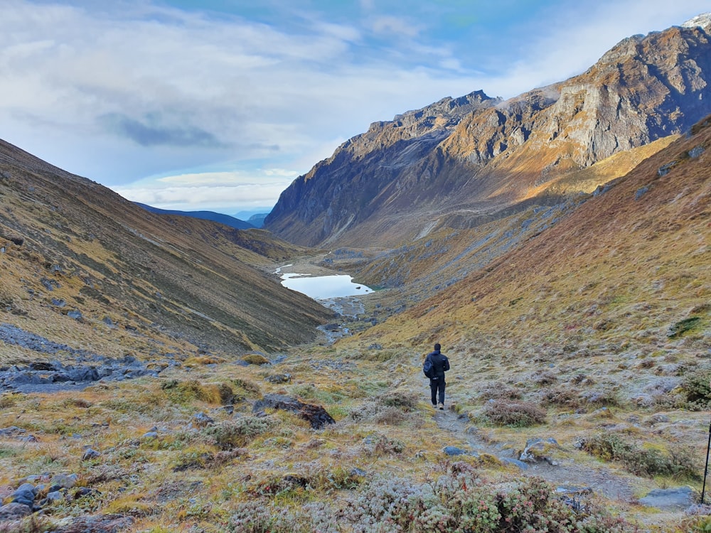 person in black jacket walking on green grass field near mountain during daytime