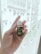 A hand is holding a small bottle labeled 'Stress Away Essential Oil Blend' against a blurred background of a building exterior. The focus is on the bottle, which has a dark green label and white cap.