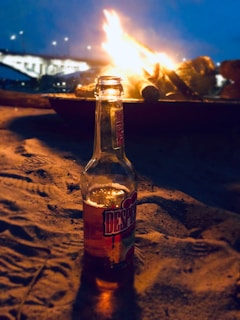 An elegant rose gold water bottle beside a cozy campfire under a starry night sky.