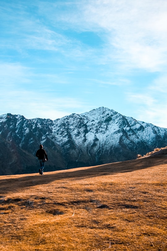 person walking on brown field near mountain during daytime in Queenstown New Zealand