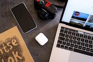 An elegant flat lay of a laptop, smartphone, and a gold-accented notebook on a black and white desk, representing a creative workspace.