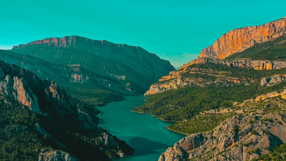 montañas verdes y marrones al lado del río bajo el cielo azul durante el día