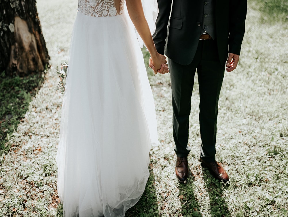 woman in white wedding gown and man in black suit standing on green grass during daytime