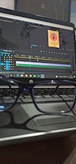 A pair of glasses is resting on a laptop keyboard. The laptop screen displays video editing software with a project timeline and a small image thumbnail labeled 'Sound On Podcast'.