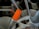 A close-up of various kitchen utensils in a holder. There are metal spoons, forks, and a brush visible. A group of bright orange chopsticks stands out prominently among the utensils.