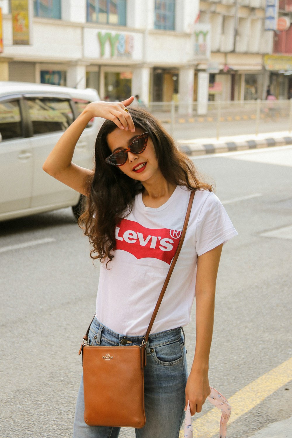 Mujer con camiseta blanca y roja de cuello redondo y jeans de mezclilla azules de pie en la carretera