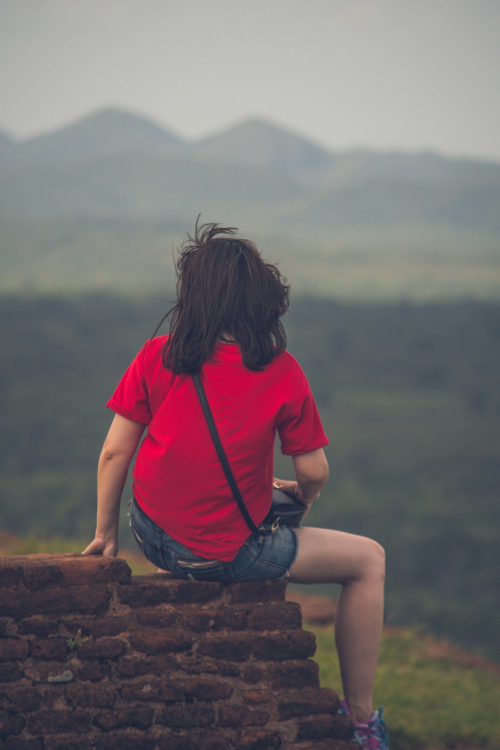 woman in red t-shirt sitting on brown rock during daytime